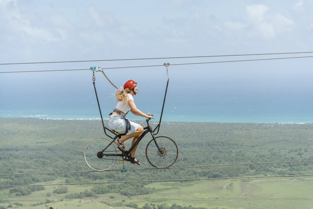 Helmeted visitor on a suspended bicycle above the coastal landscape at Montaña Redonda