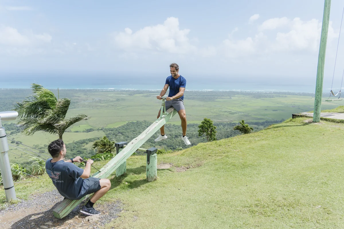 Two visitors on a hilltop seesaw overlooking the coast at Montaña Redonda
