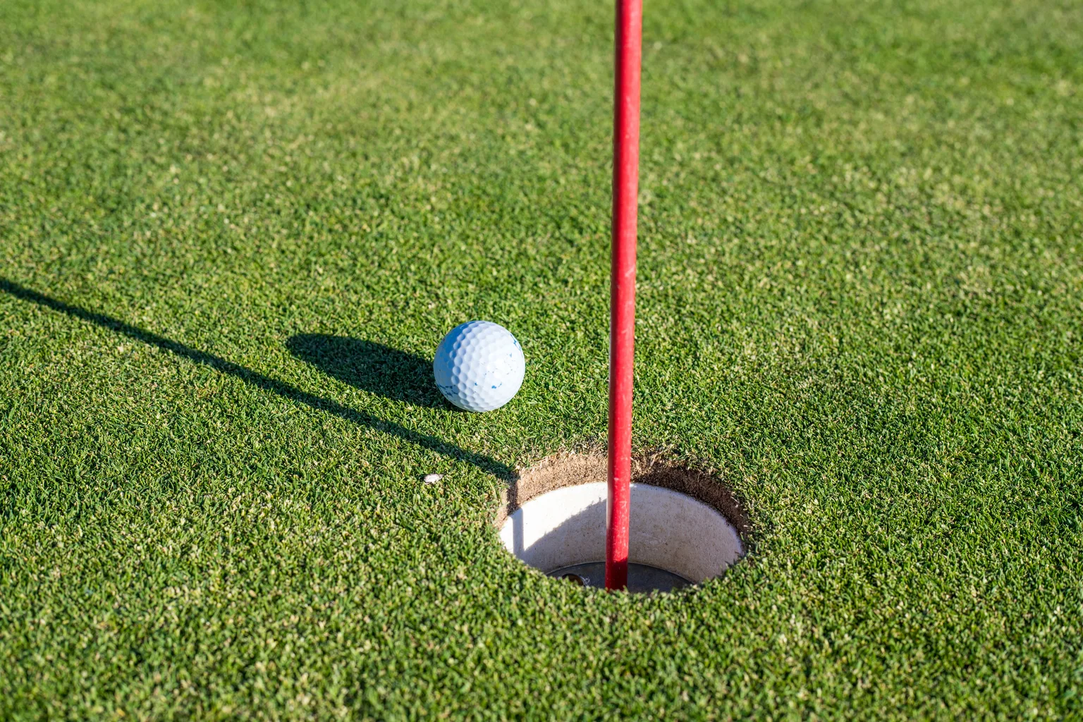 Golf ball near a hole and flag on a green