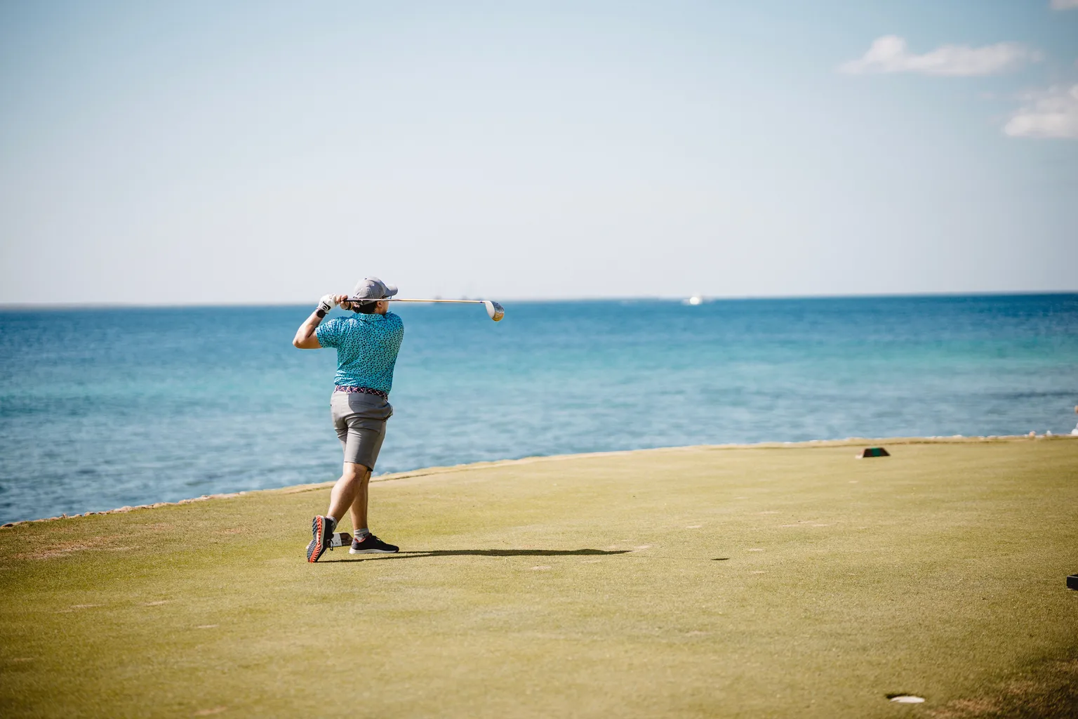 Golfer teeing off beside the sea on a coastal course