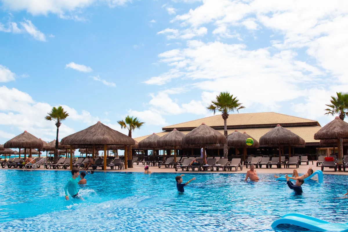 People swimming in a resort pool beside thatched umbrellas