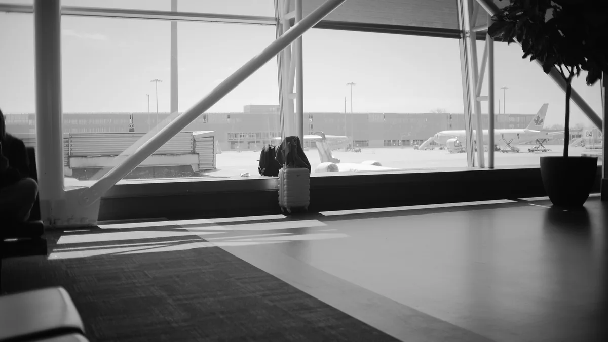 Suitcase beside large airport lounge windows in black and white