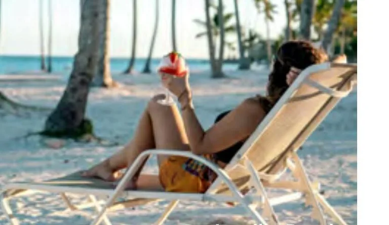 Guest resting in a beach lounger beneath palm trees at Playa Juanillo